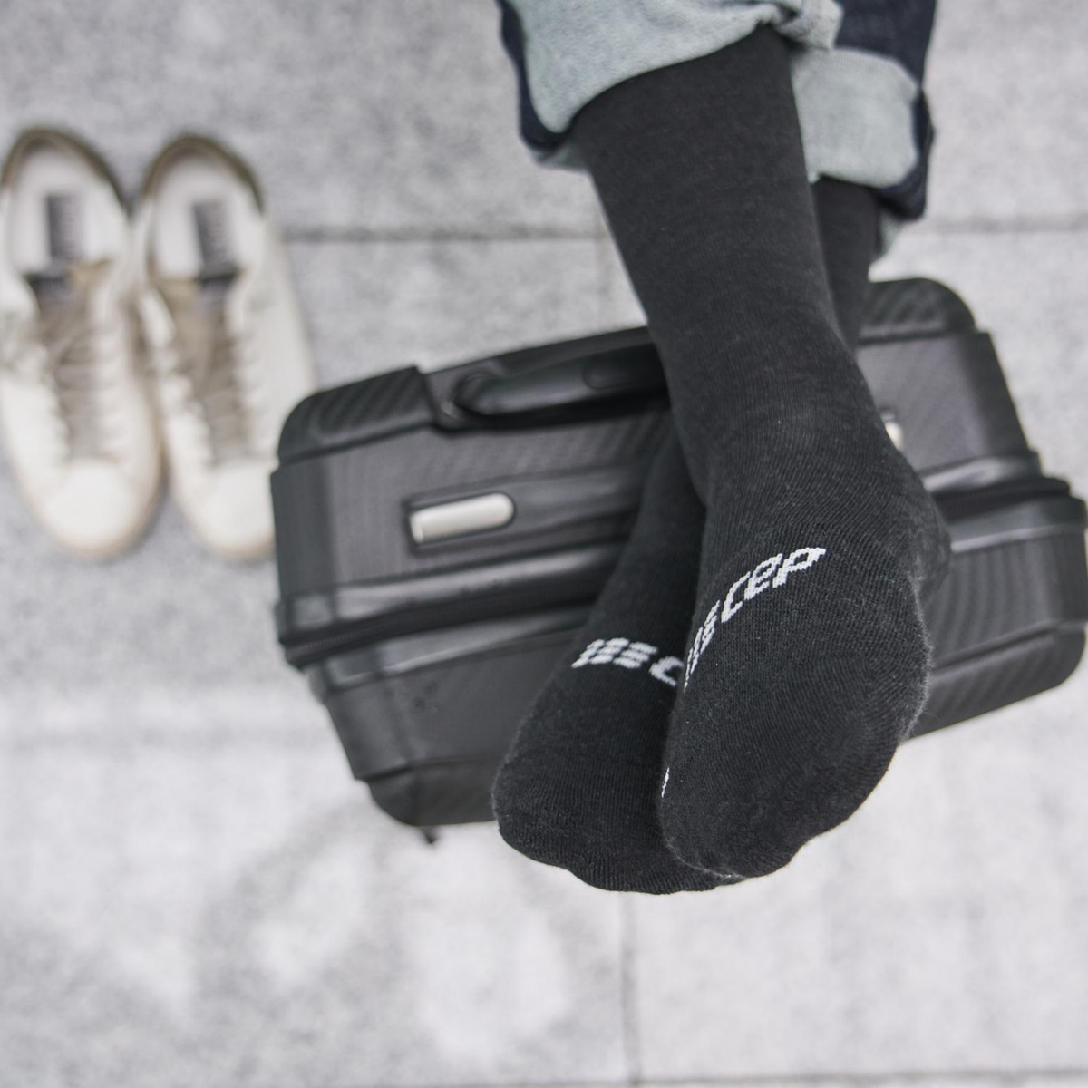 Compression flight socks in black worn on a foot resting on a suitcase, with sneakers visible in the background