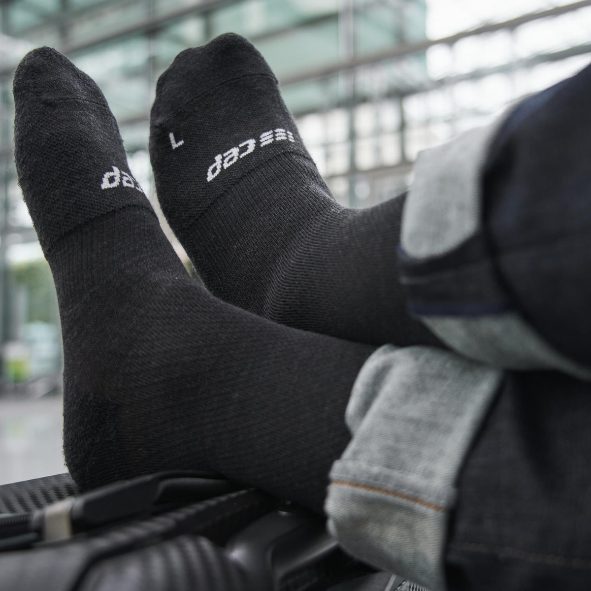 Compression flight socks in black worn on both feet, shown from the side with jeans, size L visible on cuff