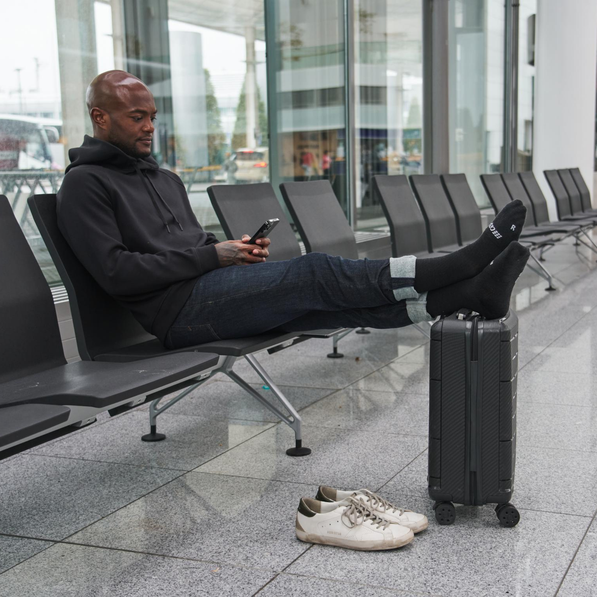 Compression flight socks in black worn by a man resting feet on luggage in an airport terminal seating area