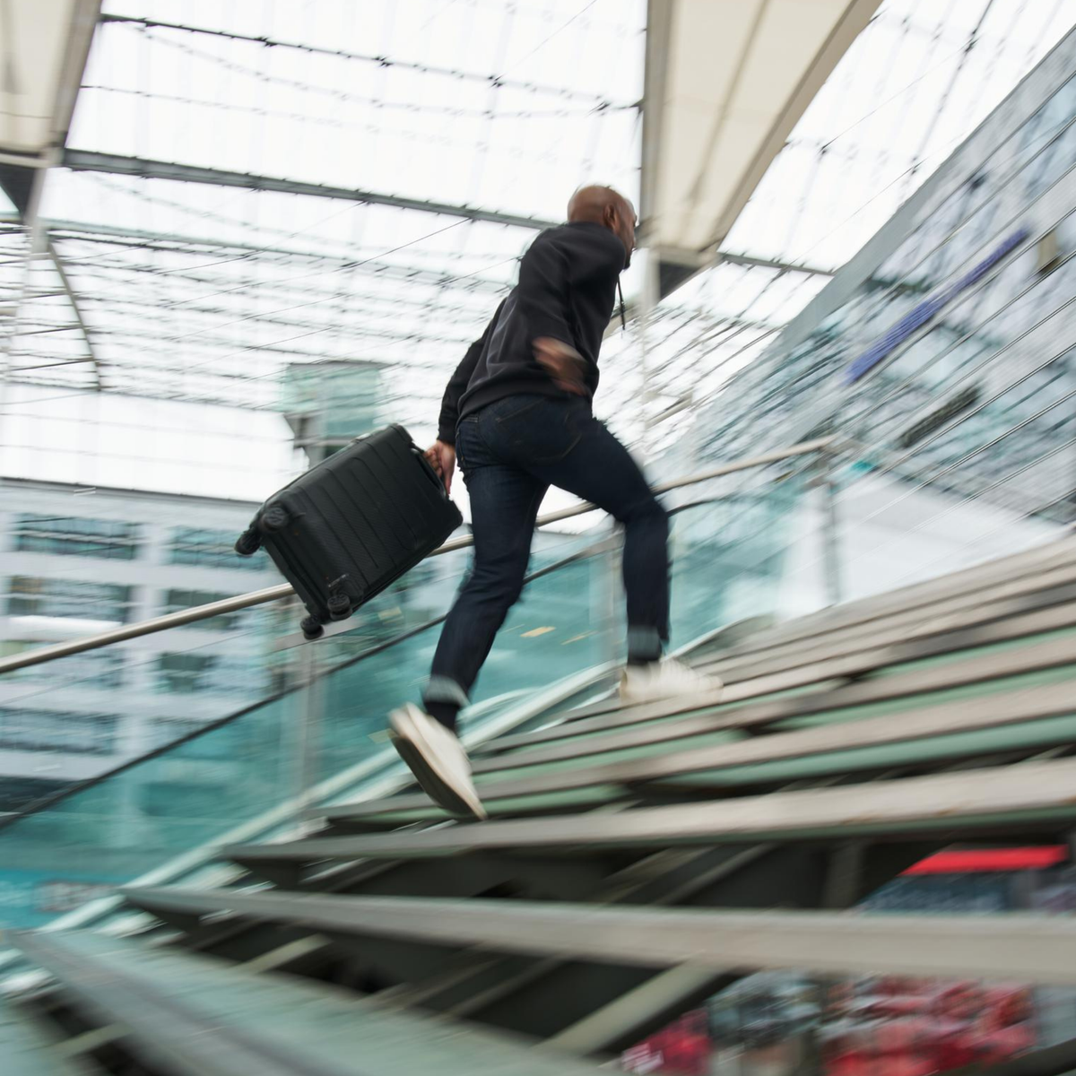 Flight socks lifestyle shot showing a man rushing up airport stairs carrying a black carry-on suitcase in a modern terminal
