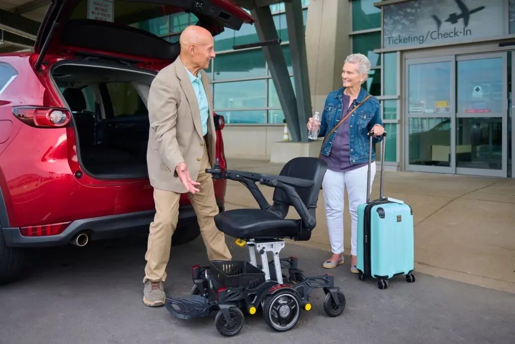 Power wheelchair being unloaded from SUV trunk at airport ticketing entrance by couple with luggage nearby