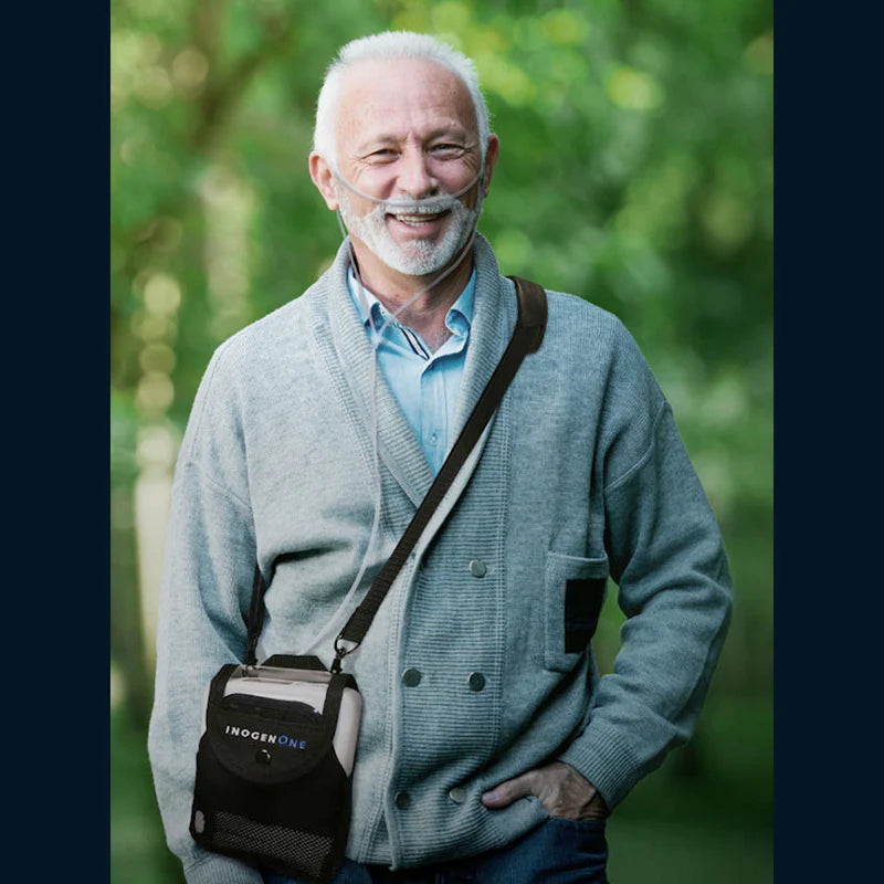 Portable oxygen concentrator worn via shoulder bag by smiling older man outdoors with nasal cannula in place