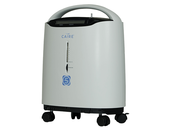 Caire stationary oxygen concentrator in light gray with top handle, front display panel, flow meter, and four rolling casters