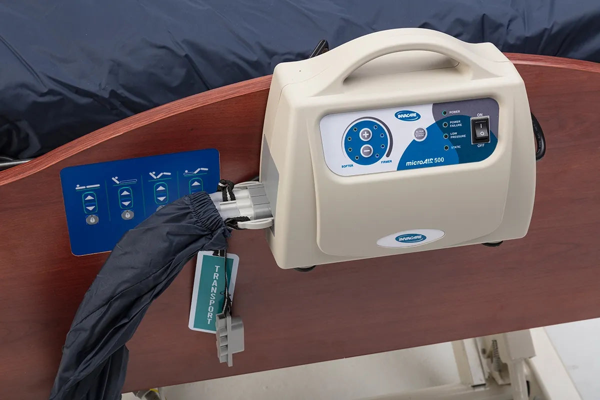 Alternating pressure mattress pump unit mounted on a hospital bed rail, connected to a dark blue mattress overlay with a