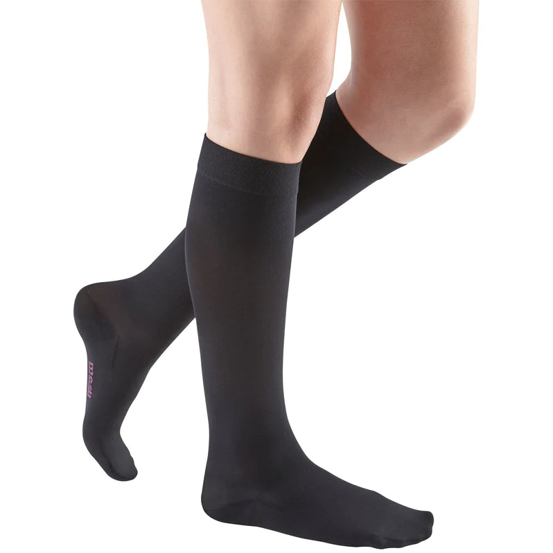 Compression knee-high stockings in black with a wide banded top, worn on a woman's legs, shown from the knees down