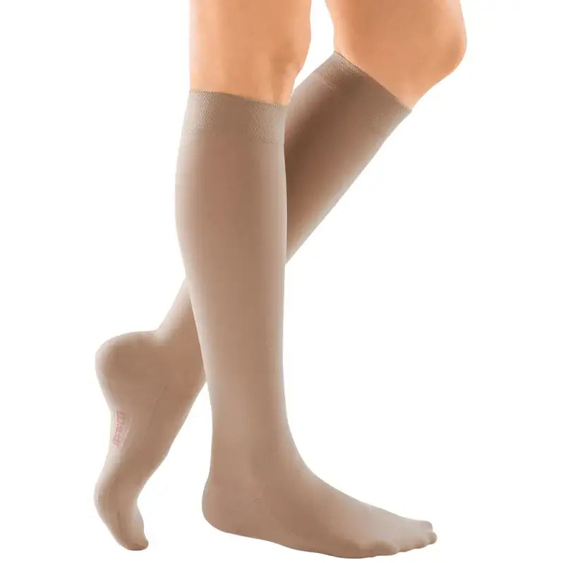 Compression stockings in beige worn on both legs, knee-high closed toe style, shown from the knees down on a white background