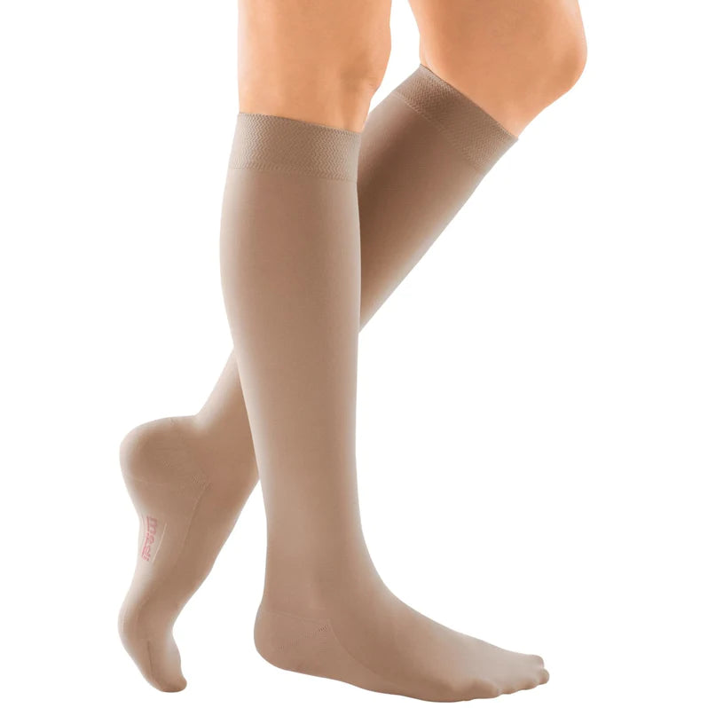 Compression stockings in beige knee-high style with wide banded top, shown on both legs against white background
