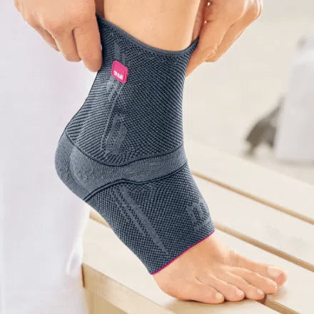Levamed ankle support in gray knit fabric with pink accents being pulled onto a foot resting on a wooden surface