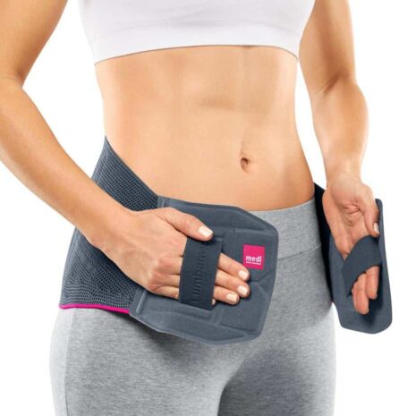 Lumbamed Plus lumbar support brace in gray with pink trim worn by a woman, shown from front with hands adjusting side panels
