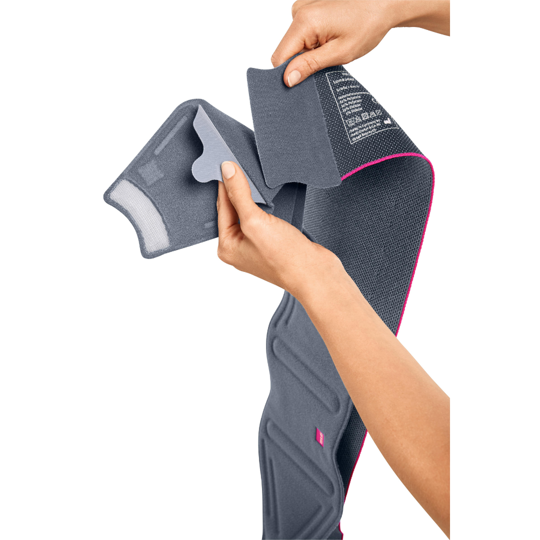 Lumbamed Sacro back support being opened by two hands to show interior padding and hook-and-loop closure, gray with pink trim