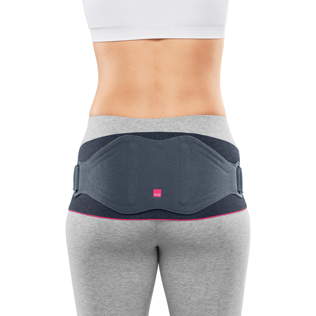Lumbamed Sacro back support belt in dark gray with pink trim, worn on a woman's lower back, rear view