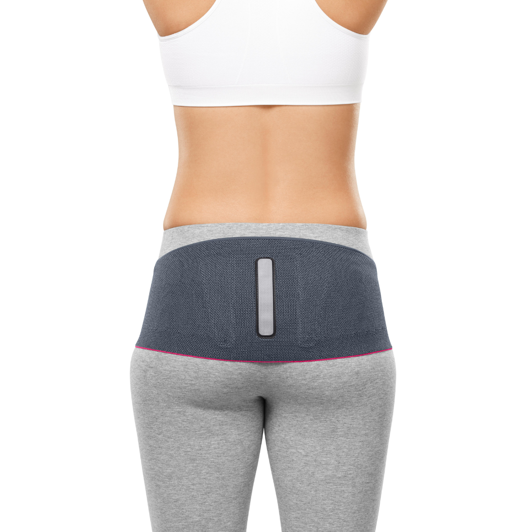 Lumbamed Sacro Support sacral belt shown from behind on a woman, featuring dark gray knit fabric with a center back pad