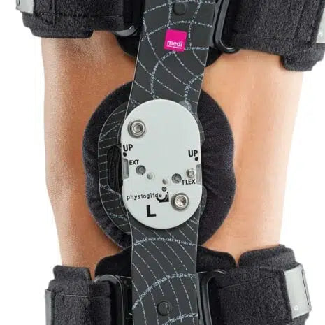Hinged knee brace with adjustable flexion and extension dial worn on a bent knee, showing side hinge mechanism and padded