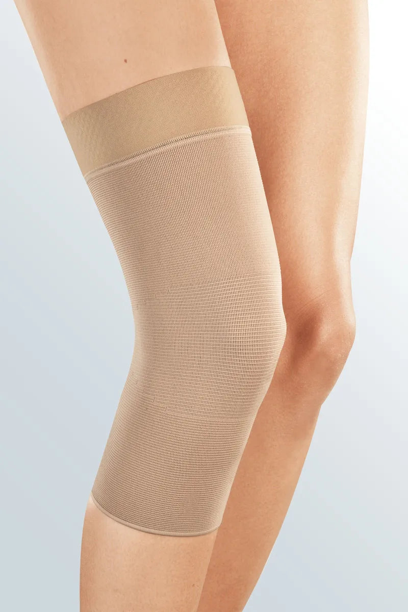 Doc Ortho Seamless Knee Support sleeve in beige knit fabric worn on a person's left knee, front view