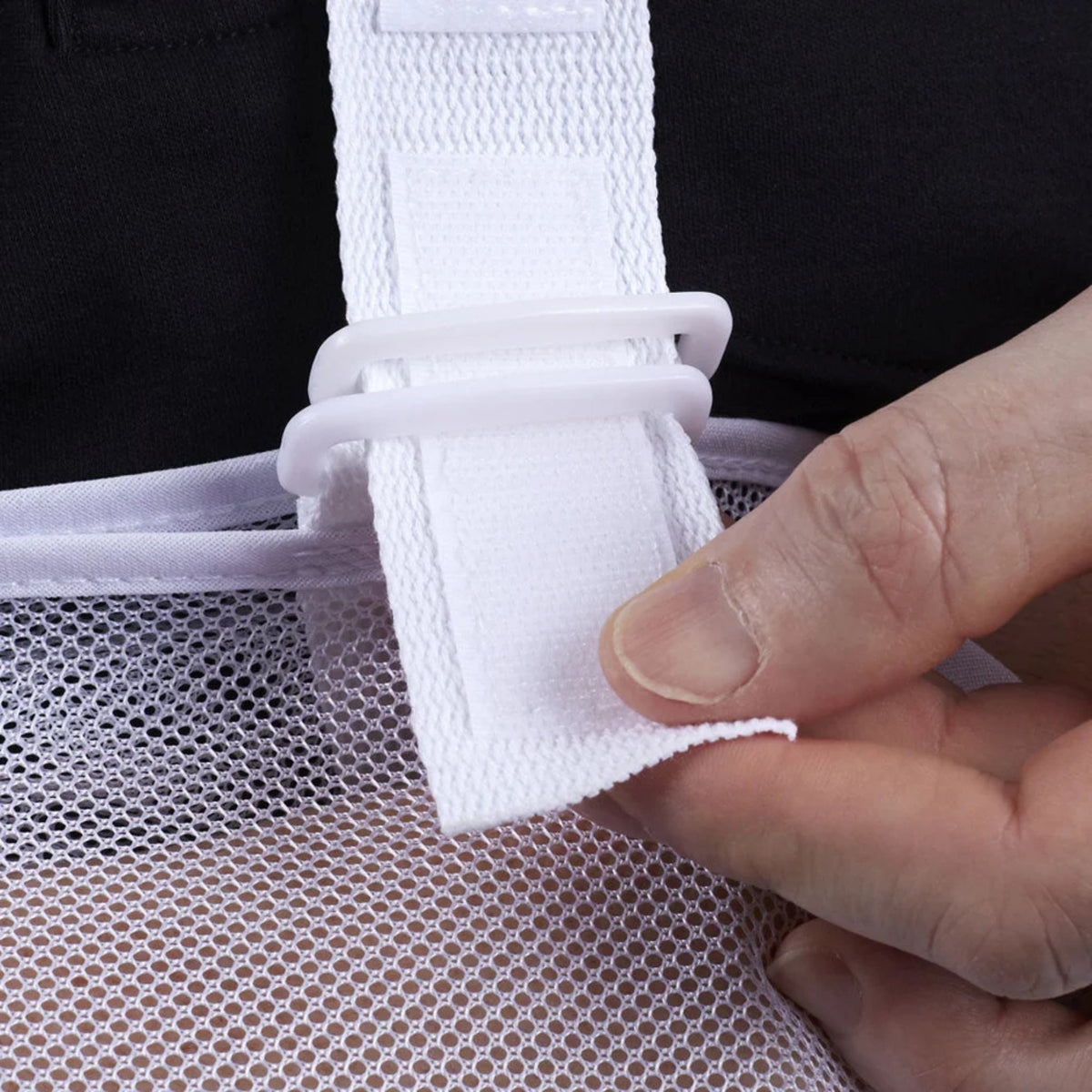 Arm sling closeup showing white mesh fabric, adjustable strap, and hook-and-loop fastener being adjusted by hand