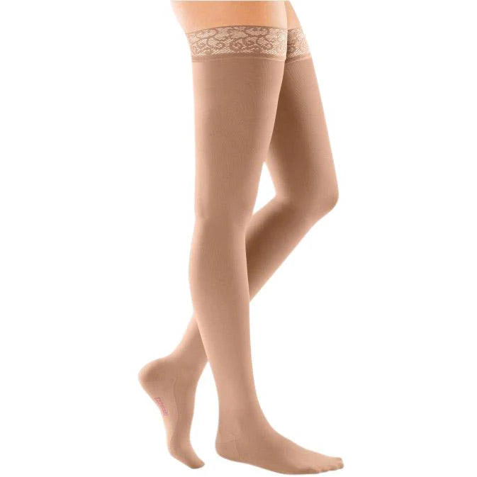 Thigh-high compression stockings in beige with decorative lace silicone top band, shown on a model's legs against white