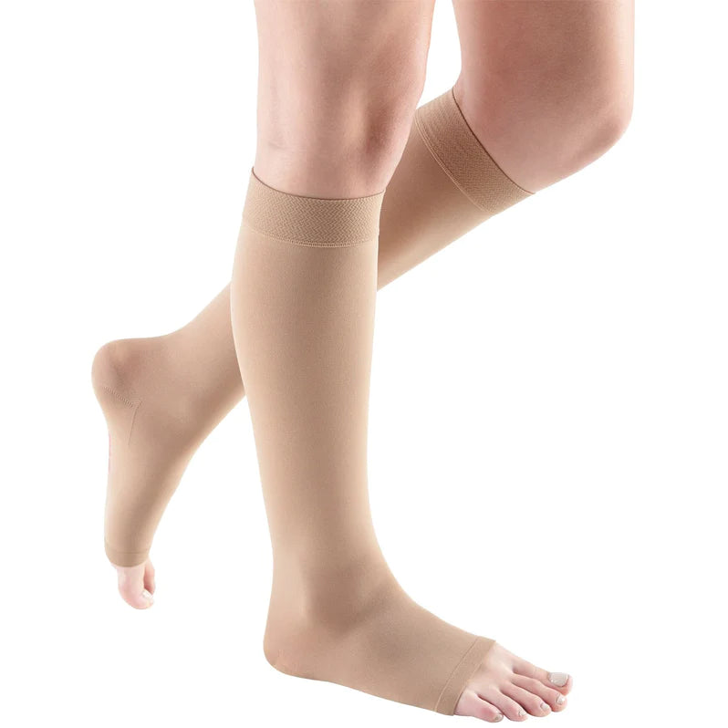 Compression stockings in beige worn on both legs, knee-high length with open toe and banded top, shown on a white background