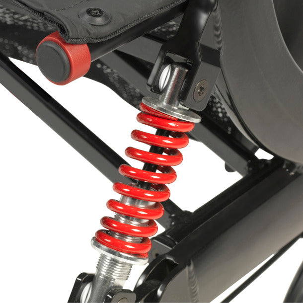 Rollator rear suspension close-up showing red coil spring shock absorber mounted on black metal frame near rear wheel