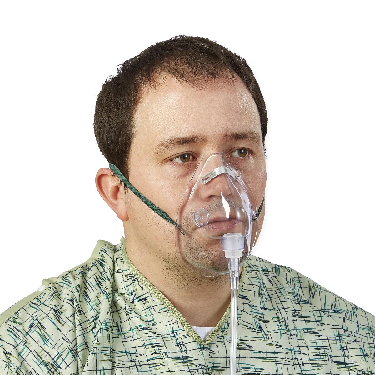 Medium concentration oxygen mask worn by a man in a hospital gown, shown with clear plastic mask, green elastic straps, and