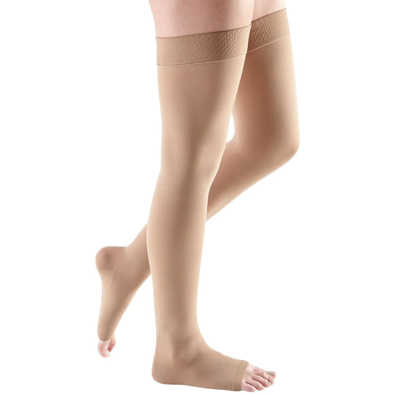 Thigh-high compression stockings in beige with open toe and silicone grip top band, shown on a model's legs against white