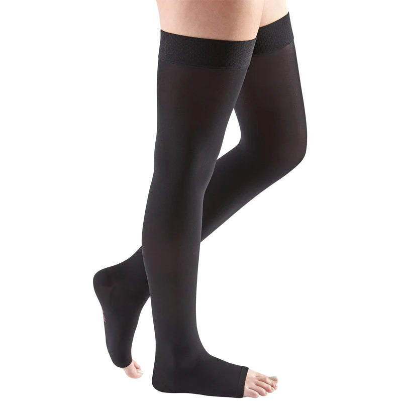 Compression thigh-high stockings in black with silicone top band and open toe, shown on a model's legs against white