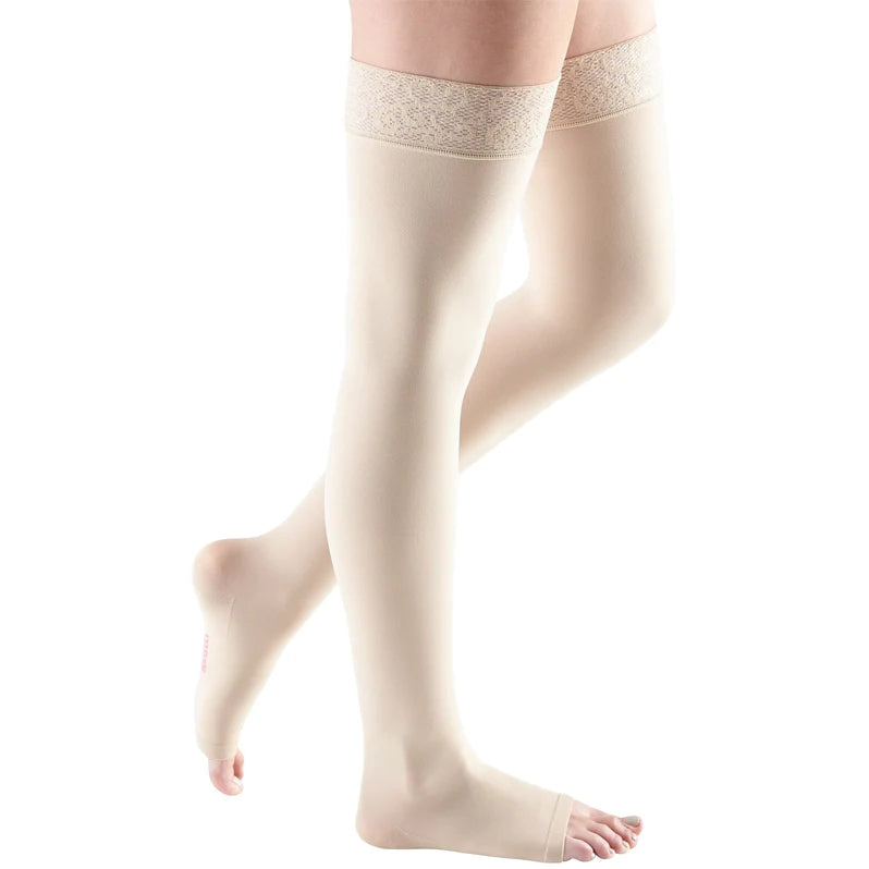 Thigh-high compression stockings in beige with lace silicone top band and open toe, shown on both legs against white