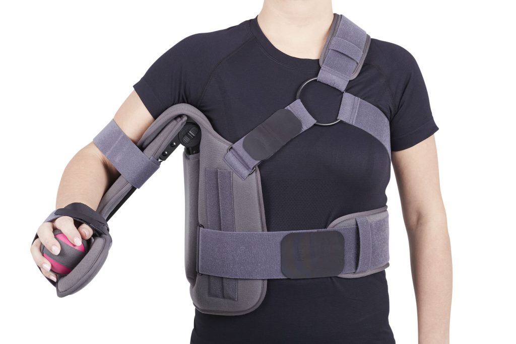 Shoulder ROM immobilizer brace worn on left arm, gray with torso strap, elbow support, and hand grip ball
