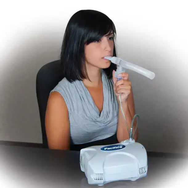 Nebulizer compressor with woman seated at table using mouthpiece connected by tubing to white Pacifica unit