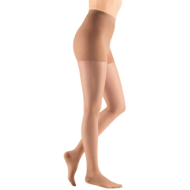 Compression pantyhose in sheer beige worn on a standing female model, side view, closed toe with waistband