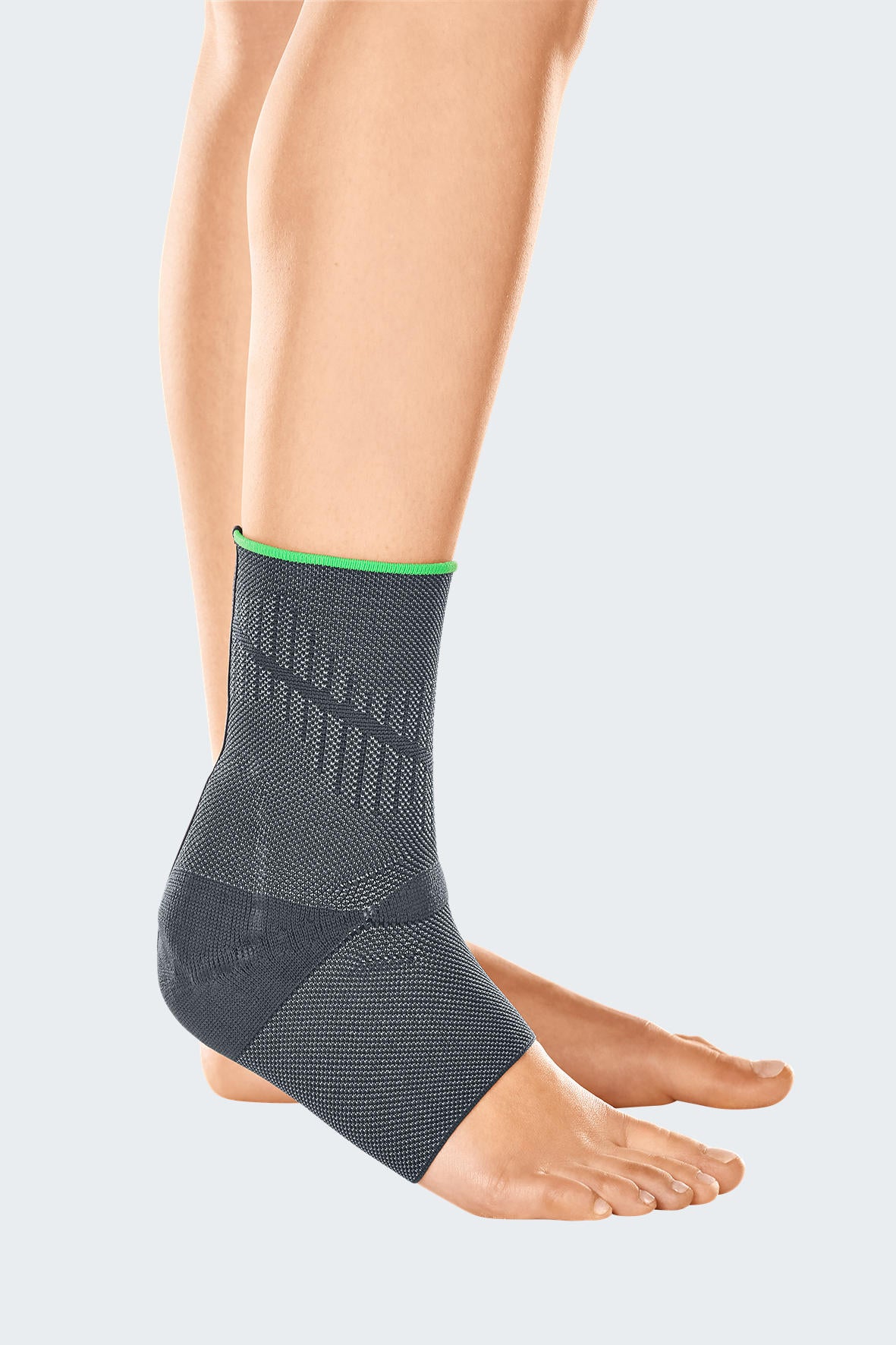 Ankle support brace in gray knit fabric with green trim and textured achilles panel, worn on left foot, side view