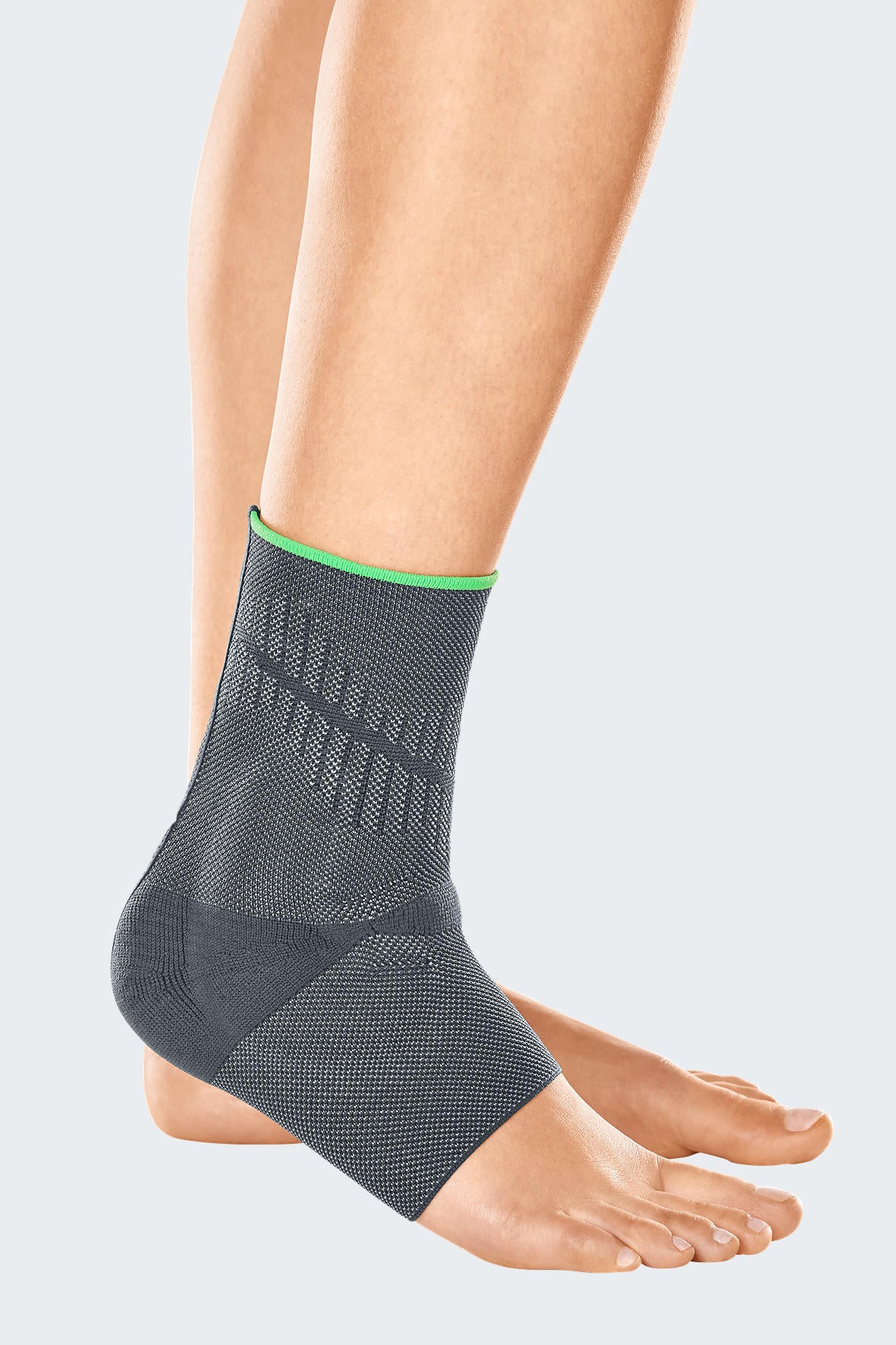 Ankle support brace in gray knit fabric with green trim band, worn on a bare foot and lower leg, side view
