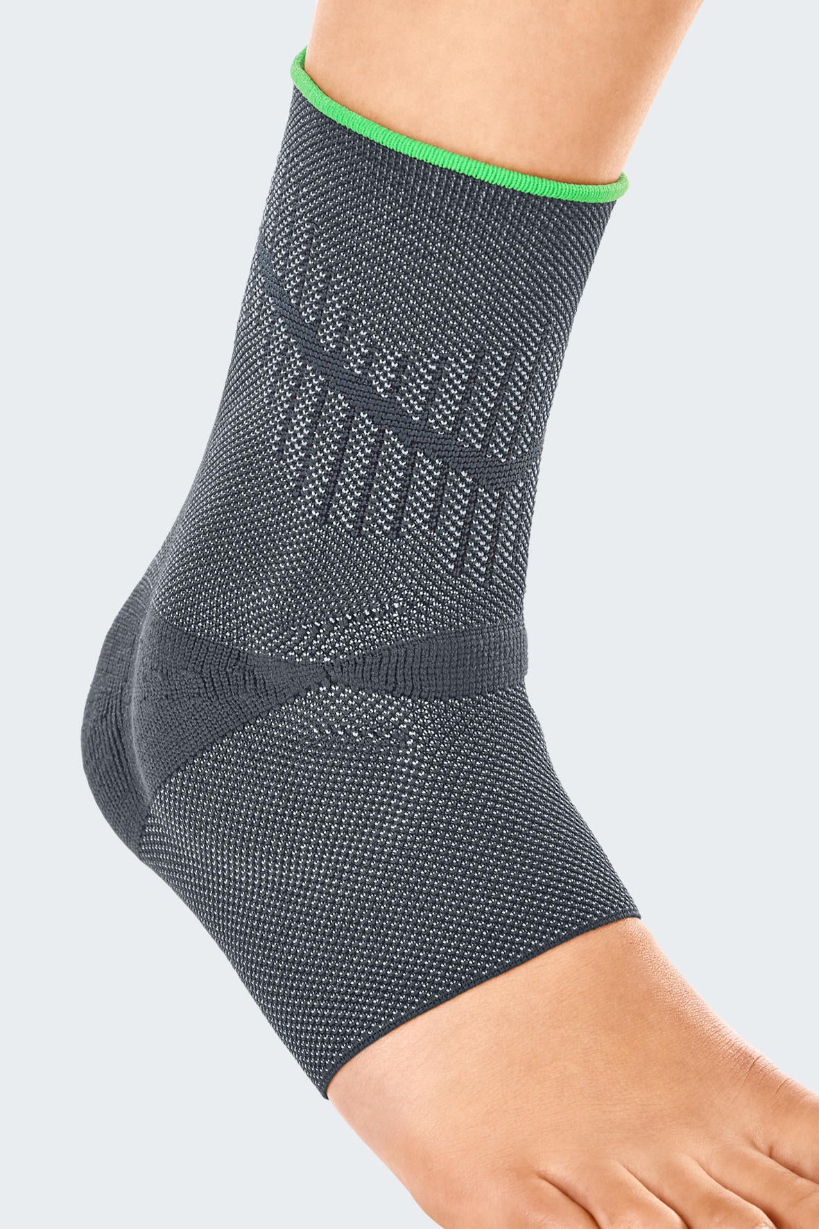 Ankle support brace in gray knit fabric with green trim and textured compression zones, worn on a bare foot and ankle