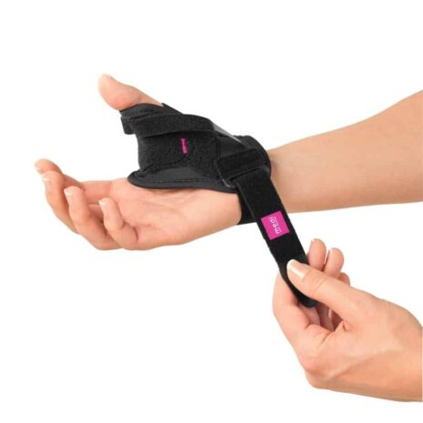 Rhizomed Soft Thumb Support being fastened onto a left hand, shown in black with pink label and adjustable strap