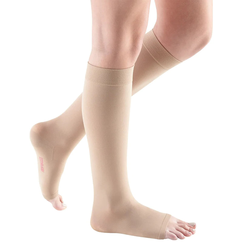 Compression stockings in beige, knee-high with open toe and wide top band, worn on both legs against white background