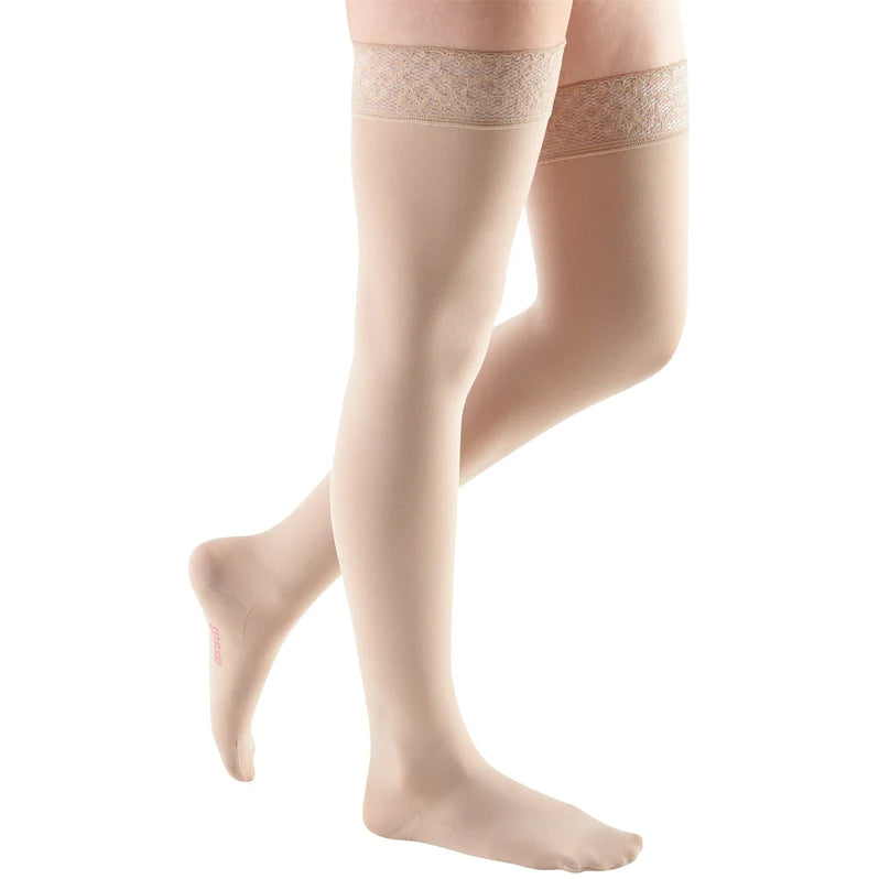 Thigh-high compression stockings in beige with lace silicone top band, shown on a model's legs against white background