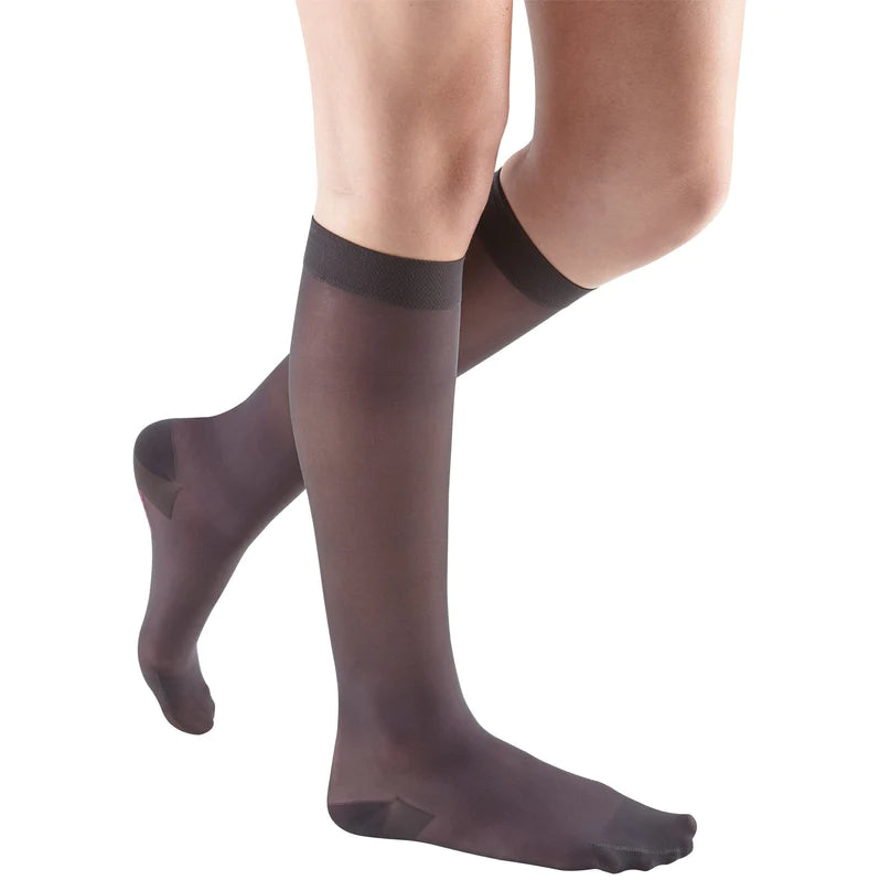 Compression knee-high stockings in sheer dark brown worn on a woman's legs, shown from the knees down against a white