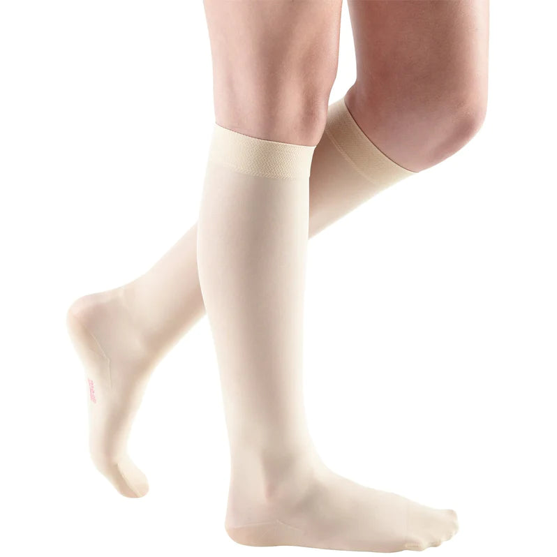 Compression stockings in beige worn on both legs, knee-high closed toe style with a knit top band