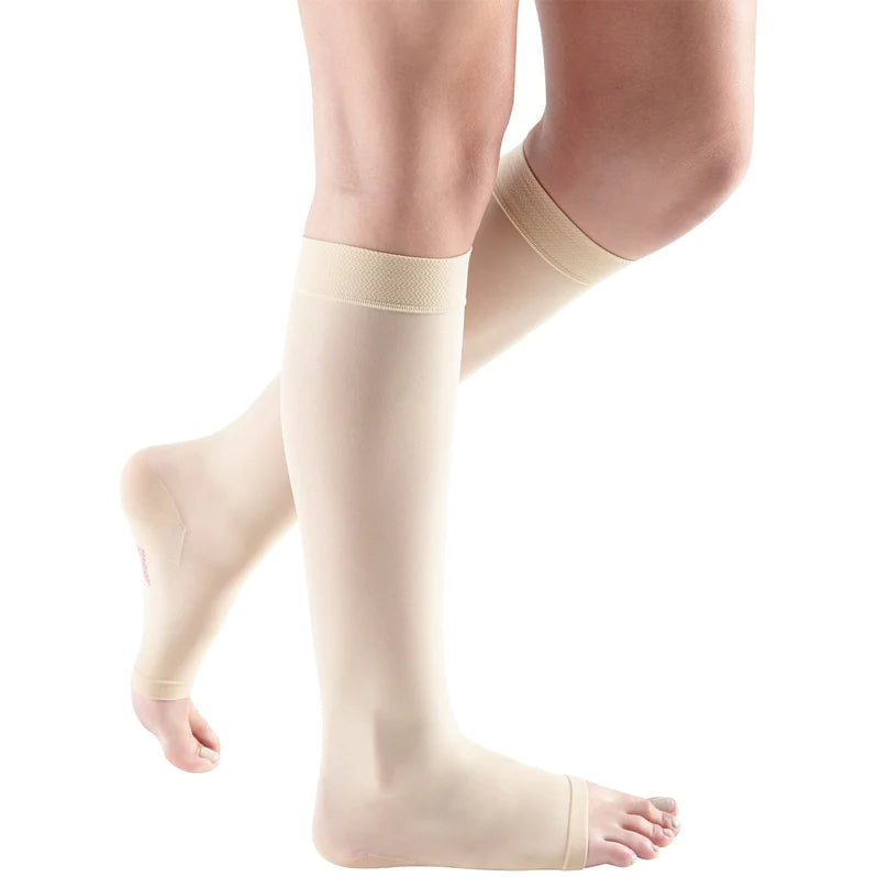 Compression stockings in beige worn on both legs, knee-high with open toe design and wide comfort top band