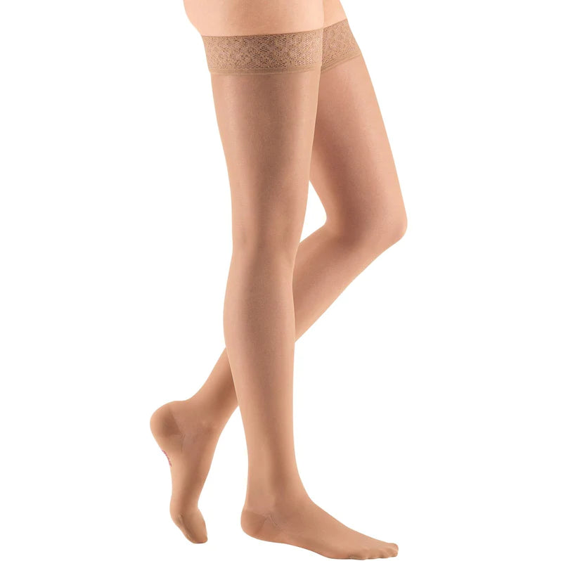 Thigh-high compression stockings in beige with lace silicone top band, shown on a model's legs against white background