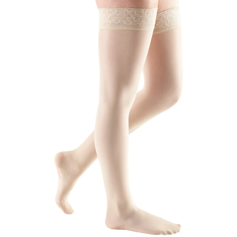 Thigh-high compression stockings in beige with lace silicone top band, closed toe, shown on a person's legs against white