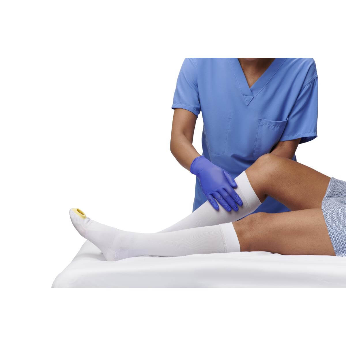 Anti-embolism knee-length compression stocking being applied to a patient's leg by a gloved clinician in blue scrubs