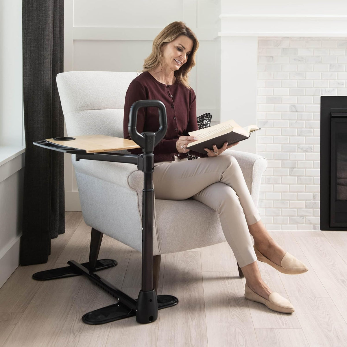 Stander Assist-A-Tray with handle and swivel tray beside a woman reading in an armchair in a living room setting