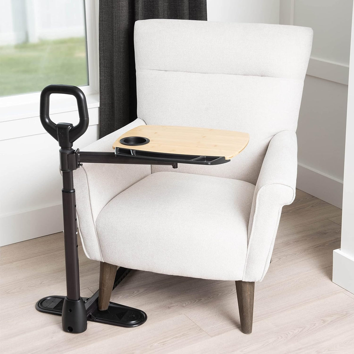 Stander floor-standing grab bar with adjustable bamboo tray and cup holder beside a white armchair