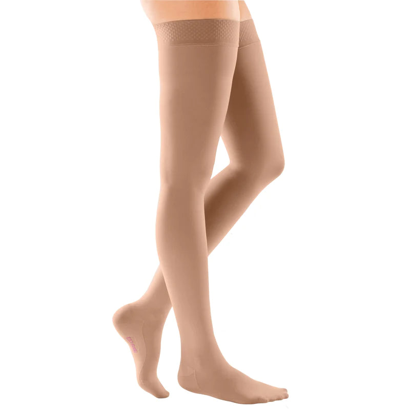 Compression thigh-high stockings in beige with silicone dot top band, shown on a model's legs against white background