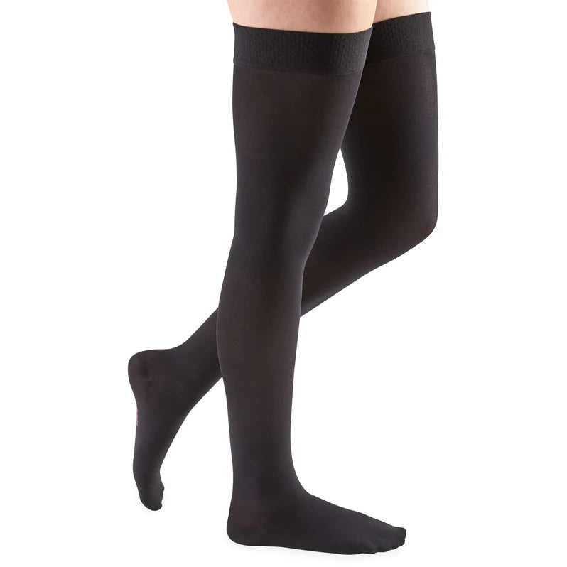 Compression thigh-high stockings in black with silicone lace top band, shown on a person's legs against white background