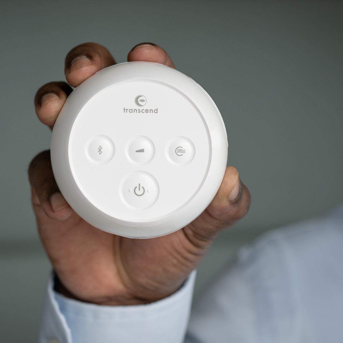 Transcend Micro Auto CPAP machine held in hand, showing round white top panel with power, Bluetooth, and settings buttons