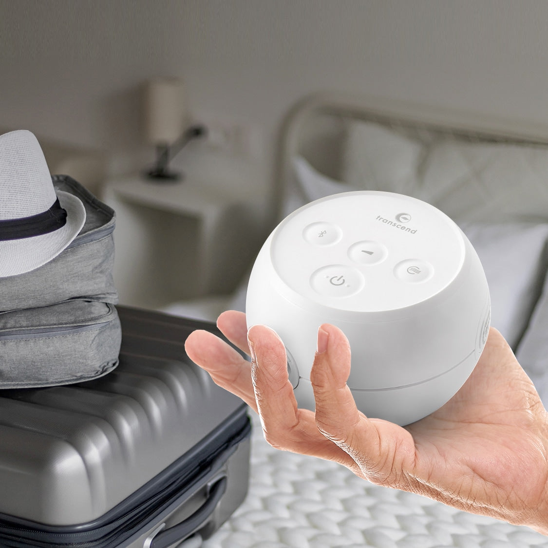 Transcend Micro Auto CPAP machine held in one hand beside packed luggage in a bedroom setting