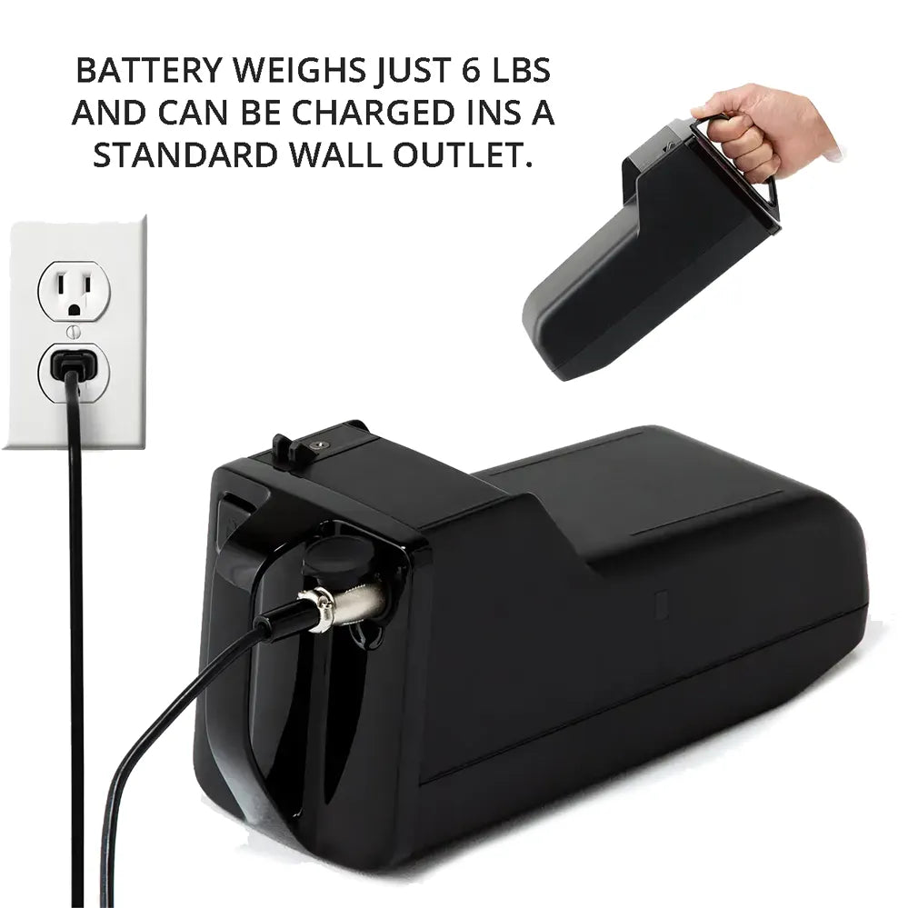 Power wheelchair battery pack plugged into standard wall outlet, with hand holding detached battery showing carry handle