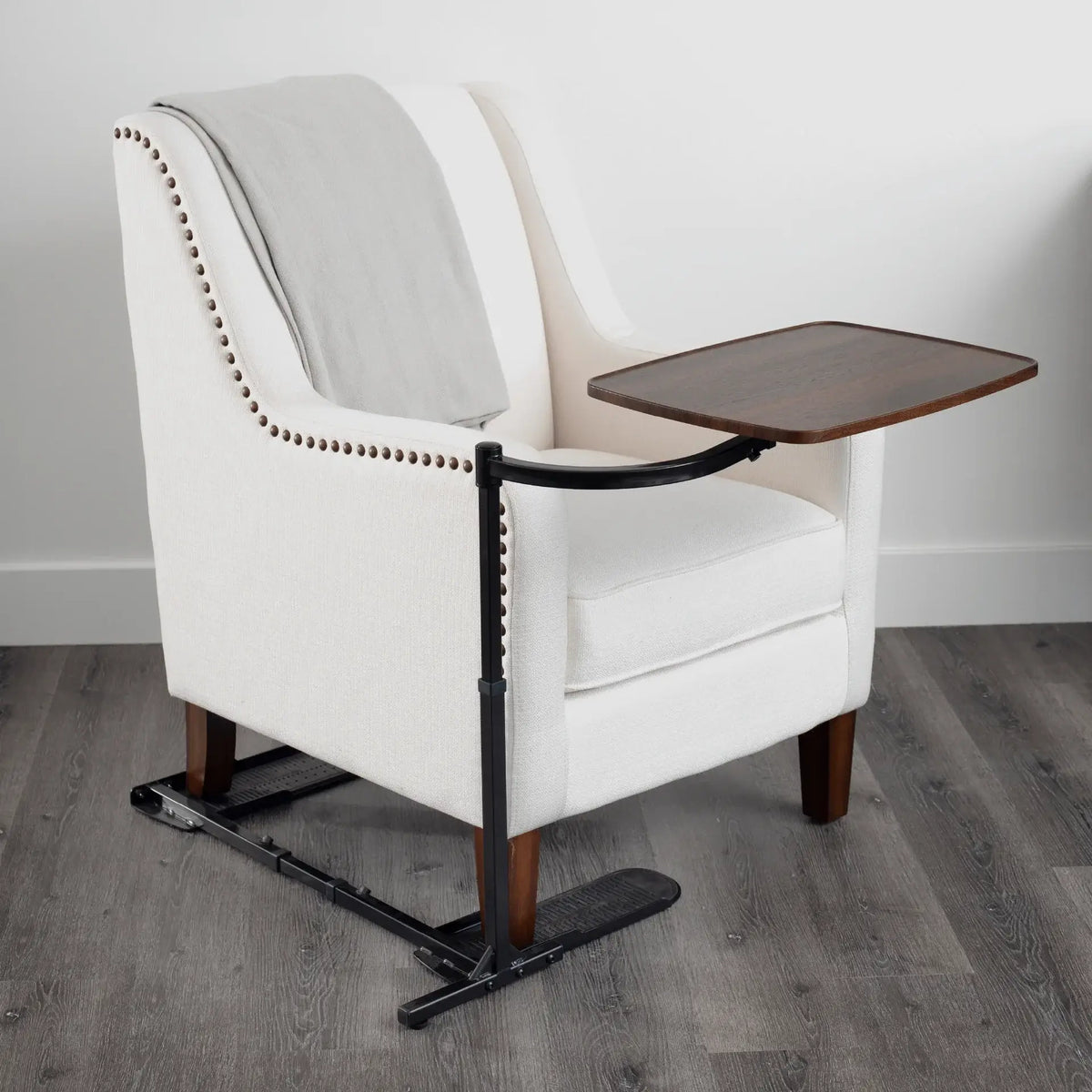 Chair tray table with black metal adjustable arm and walnut-finish wooden surface, shown mounted beside a white upholstered