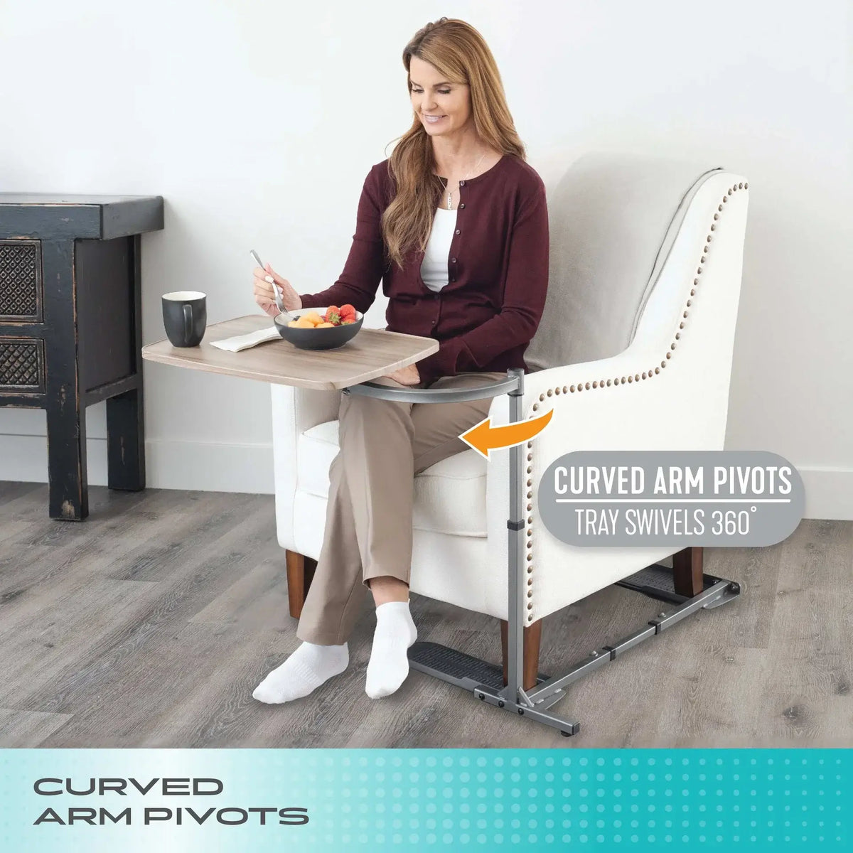Swivel tray table with curved arm pivots positioned beside a seated woman eating from a bowl in a white armchair
